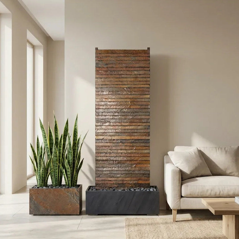 AVA GRANDE Wasserwand aus Schiefer Rusty in einem hellen Wohnzimmer neben einem Sofa, daneben ein Pflanzgefäss mit Bogenhanf - CLIMAQUA (KI-Inhalte)