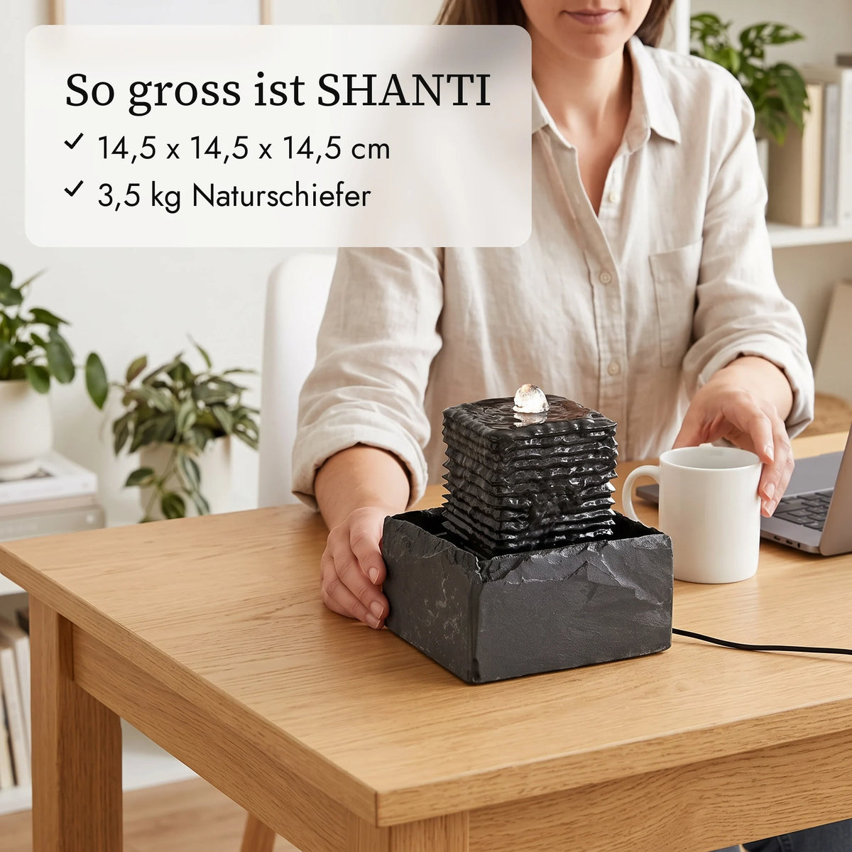 So gross ist SHANTI: Zimmerbrunnen 14,5 cm neben Kaffeetasse und Hand auf dem Schreibtisch (KI-Inhalte)
