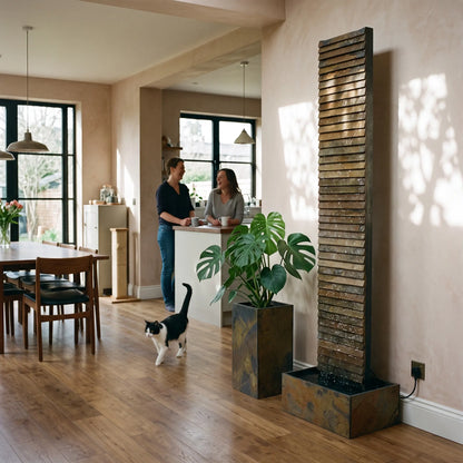 CLIMAQUA AVA XL Wasserwand aus Schiefer in einer offenen Wohnküche, daneben ein PYLO 60 Pflanzgefäss mit Monstera - CLIMAQUA (KI-Inhalte)